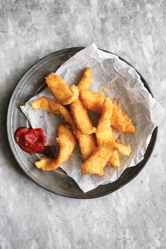 A pile of fancy fish sticks on a piece of parchment with a dollop of ketchup beside them.