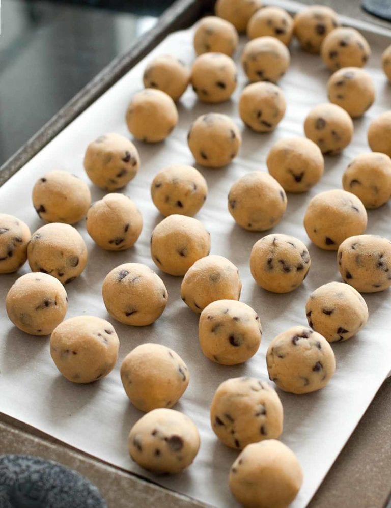 Balls of frozen chocolate chip cookie dough on a parchment-lined baking sheet.