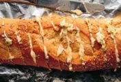 A loaf of garlic bread, cut into deep slices and covered in garlic butter on a piece of aluminum foil.