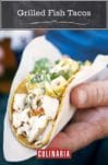 A hand holding a grilled fish taco topped with cilantro that is wrapped in a paper napkin.