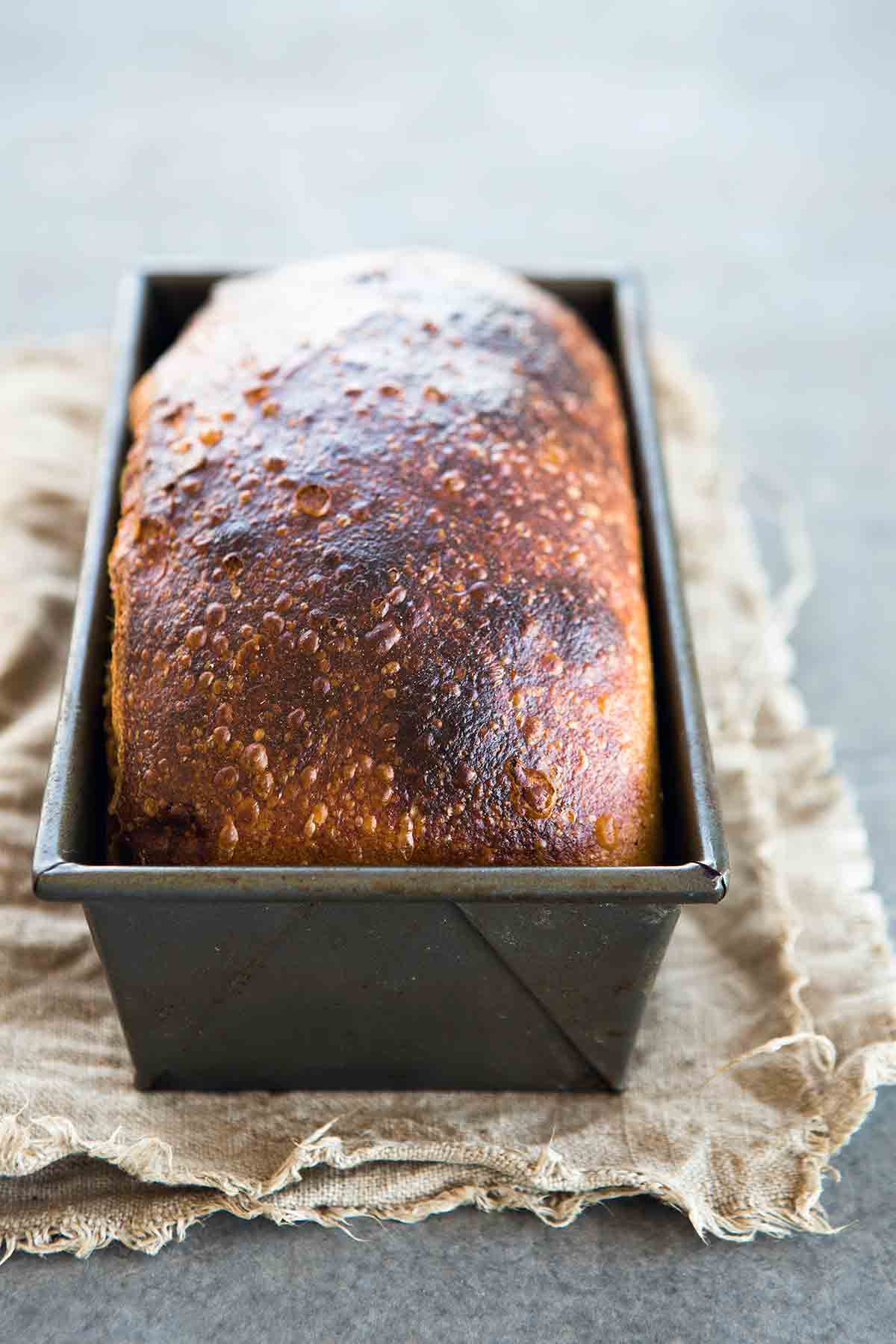 A browned loaf of homemade sandwich bread in a metal loaf tin.