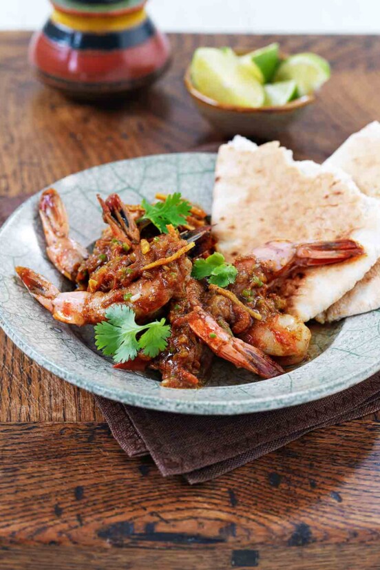 A blue-speckled bowl filled with Indian spiced shrimp, garnished with cilantro and served with flatbread.