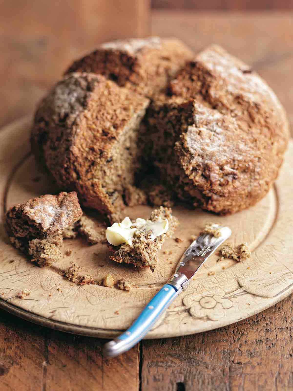 A loaf of Irish soda bread on a brown plate with a chunk cut out and smeared with butter.