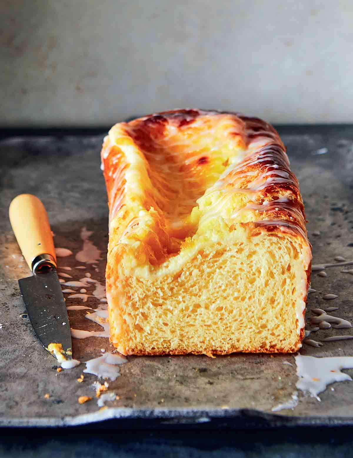 A loaf of lemon cream cheese Danish bread on a piece of foil with a knife lying beside it.