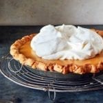 A whole maple cream pie, topped with whipped cream on a round wire rack.