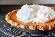 A whole maple cream pie, topped with whipped cream on a round wire rack.