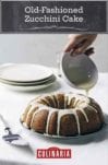 An old-fashioned zucchini cake on a silver plate with lemon glaze being drizzled over it.