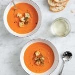 Two bowls of roasted red pepper soup, topped with croutons and thyme leaves.