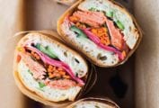 Four pieces of salmon banh mi wrapped in paper in a box.