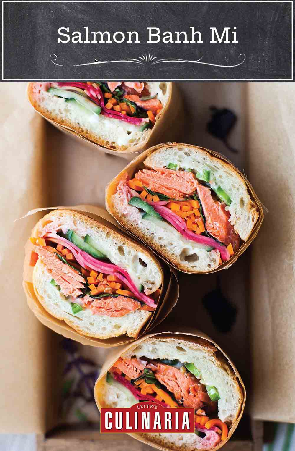 Four pieces of salmon banh mi wrapped in paper in a box.