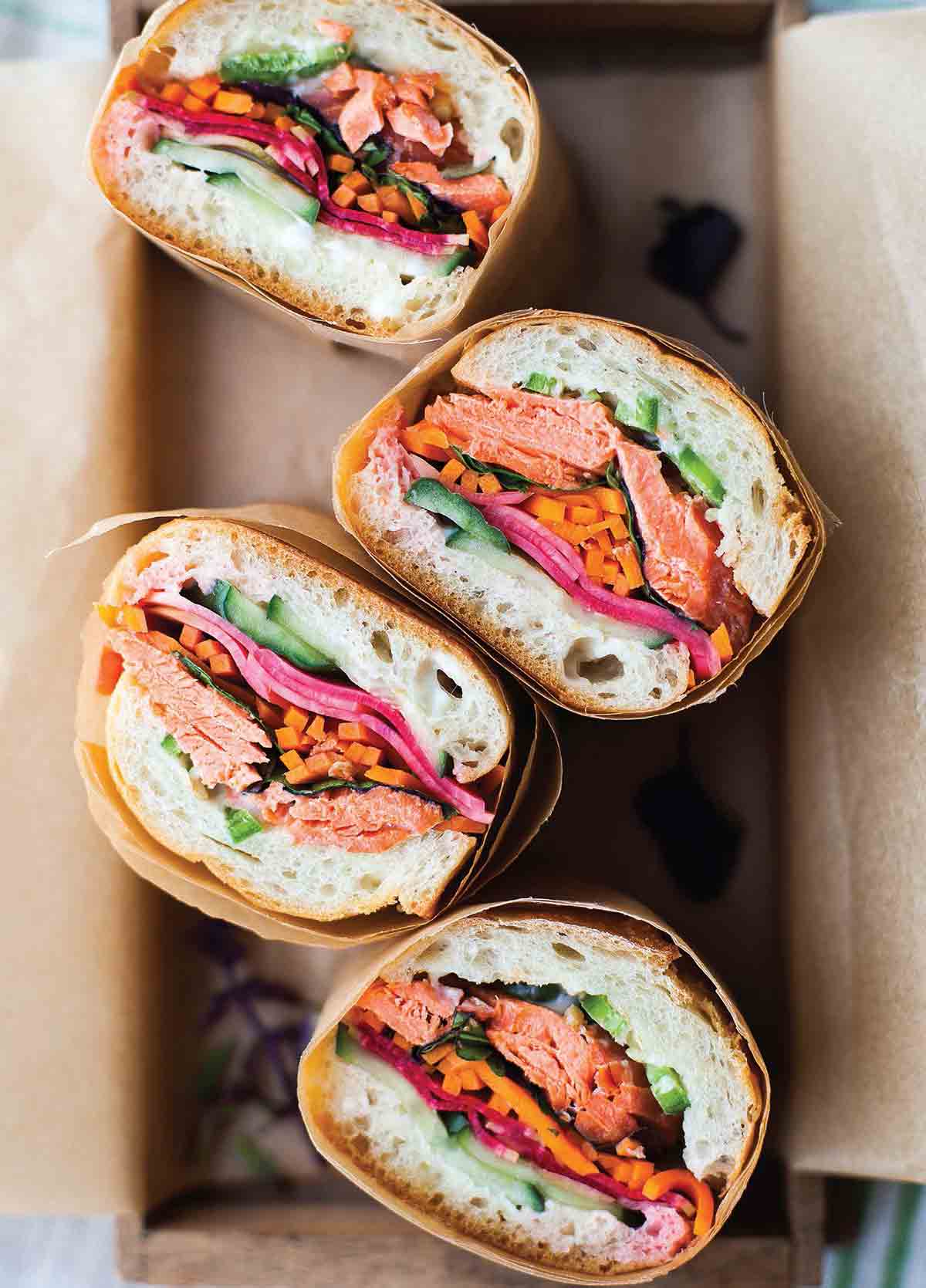 Four pieces of salmon banh mi wrapped in paper in a box.