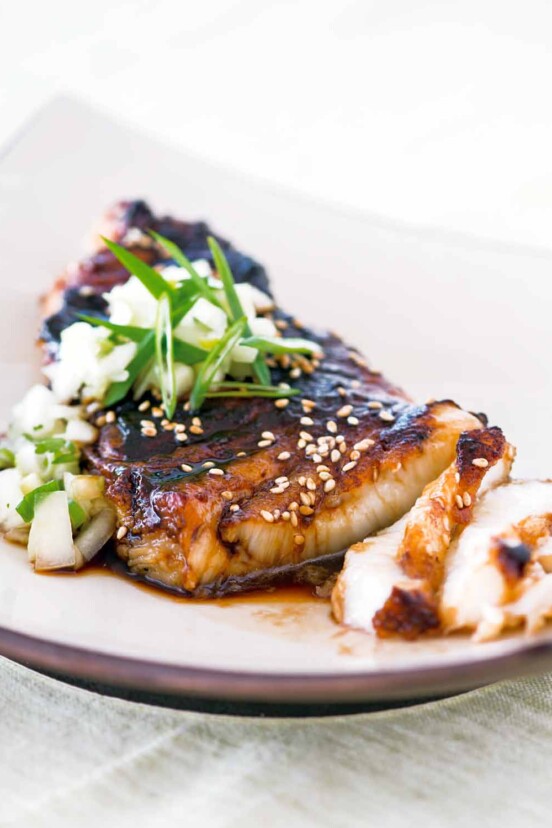 A piece of sea bass topped with soy glaze and cucumber salsa on a square shaped white plate.