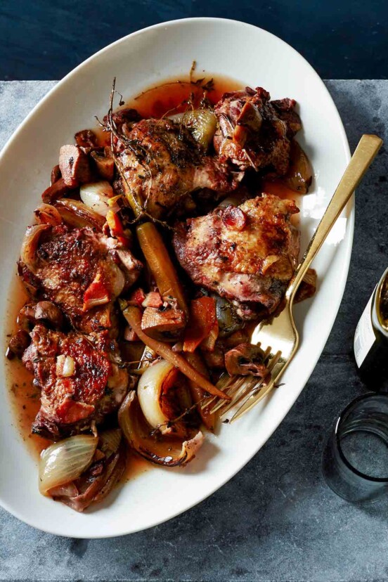 A white oval serving plate filled with slow cooker coq au vin and a gold fork resting on the side of the plate.
