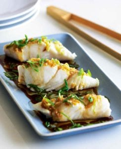 Three pieces of steamed halibut with ginger and scallions on a blue rectangular plate with chopsticks on the side.