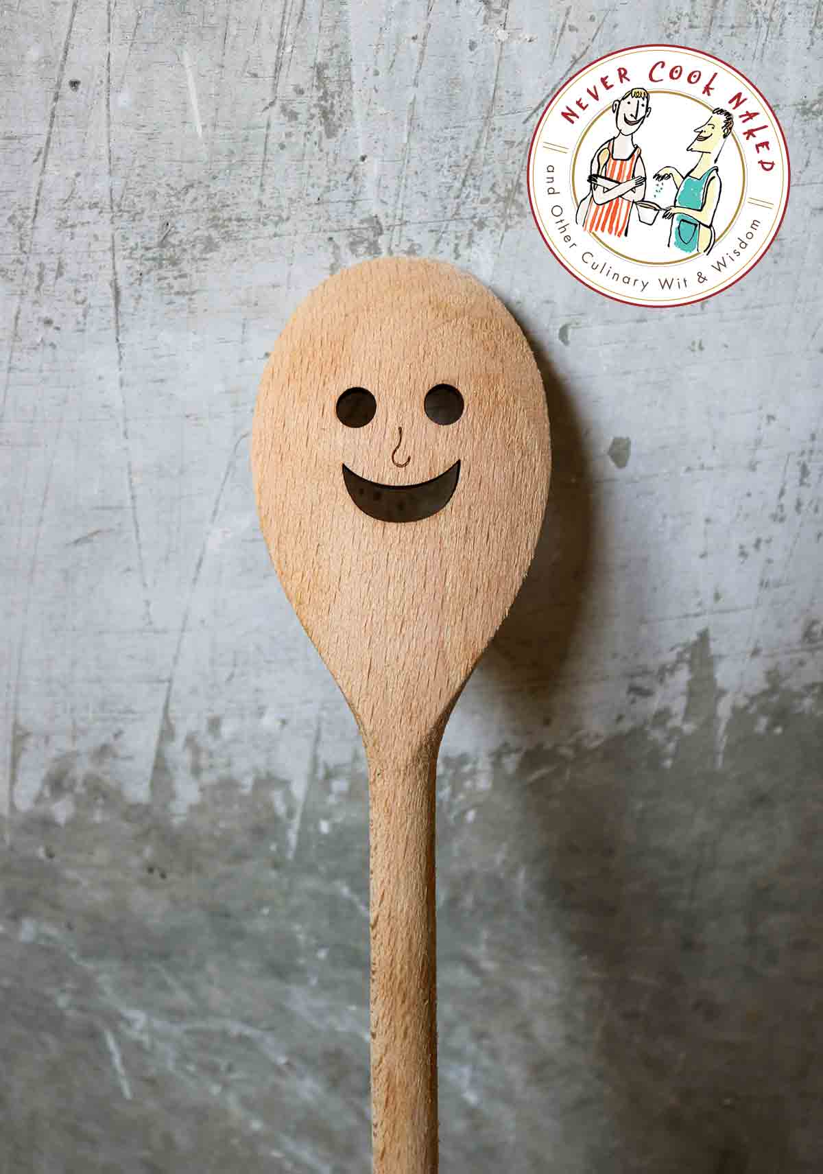 Wooden spoon with a black smiley face painted on it with a gray background.