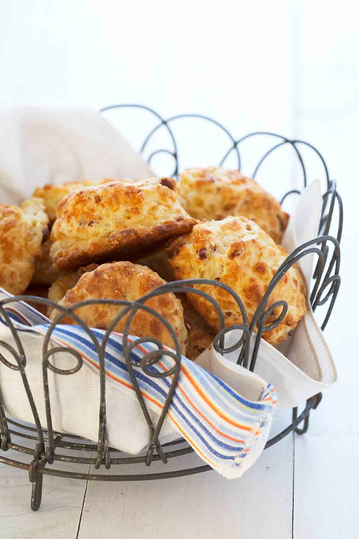 A wire basket lined with a napkin and filled with bacon Cheddar biscuits.
