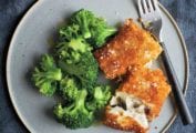 Two pieces of breaded fish fillets sprinkled with salt on a grey plate with a portion of steamed broccoli and a fork.