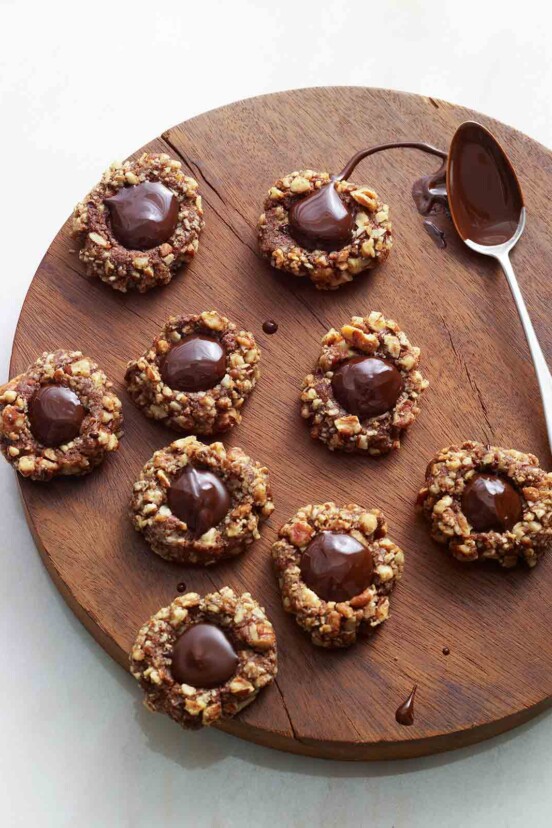 Nine chocolate thumbprint cookies and a chocolate covered spoon on a round wooden board.