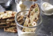Fig, apricot, and pistachio biscotti resting inside or on top of two glasses and a stack of biscotti beside the glassware.