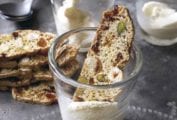 Fig, apricot, and pistachio biscotti resting inside or on top of two glasses and a stack of biscotti beside the glassware.