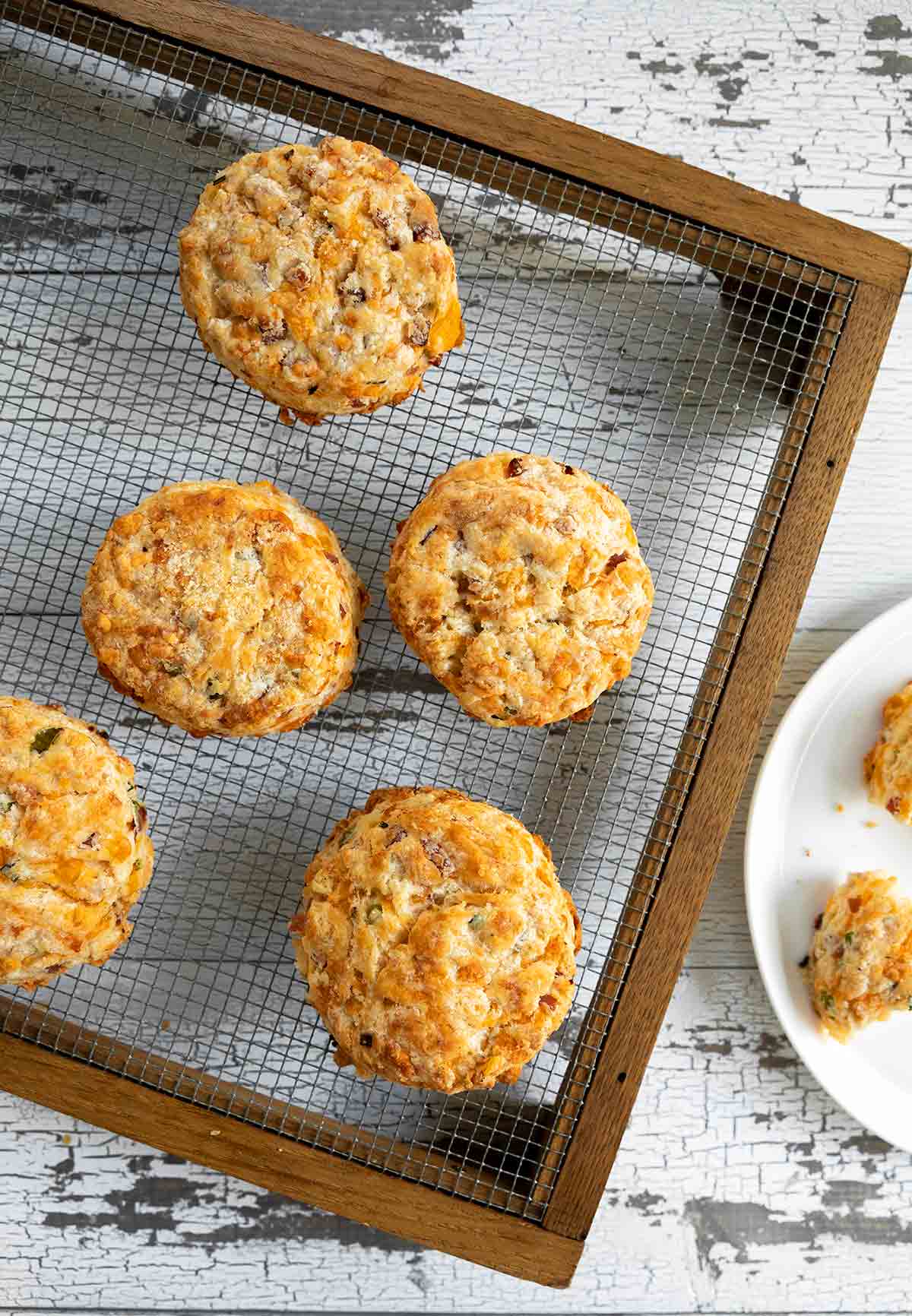 Cooling rack with 5 ham and Cheddar biscuits on it plus a white plate with a half eaten biscuit on top