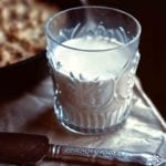 A glass half-filled with homemade almond milk with a serving knife resting in front of it.