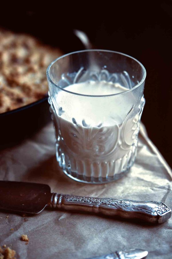 A glass half-filled with homemade almond milk with a serving knife resting in front of it.