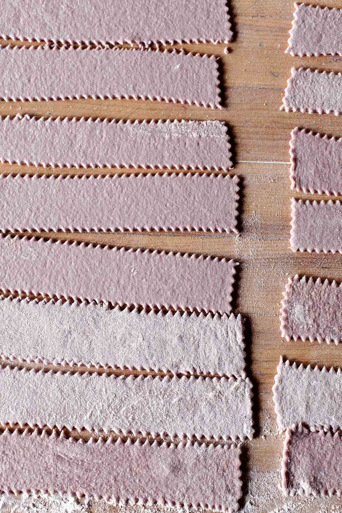 Strips of homemade red wine pasta on a wooden surface.