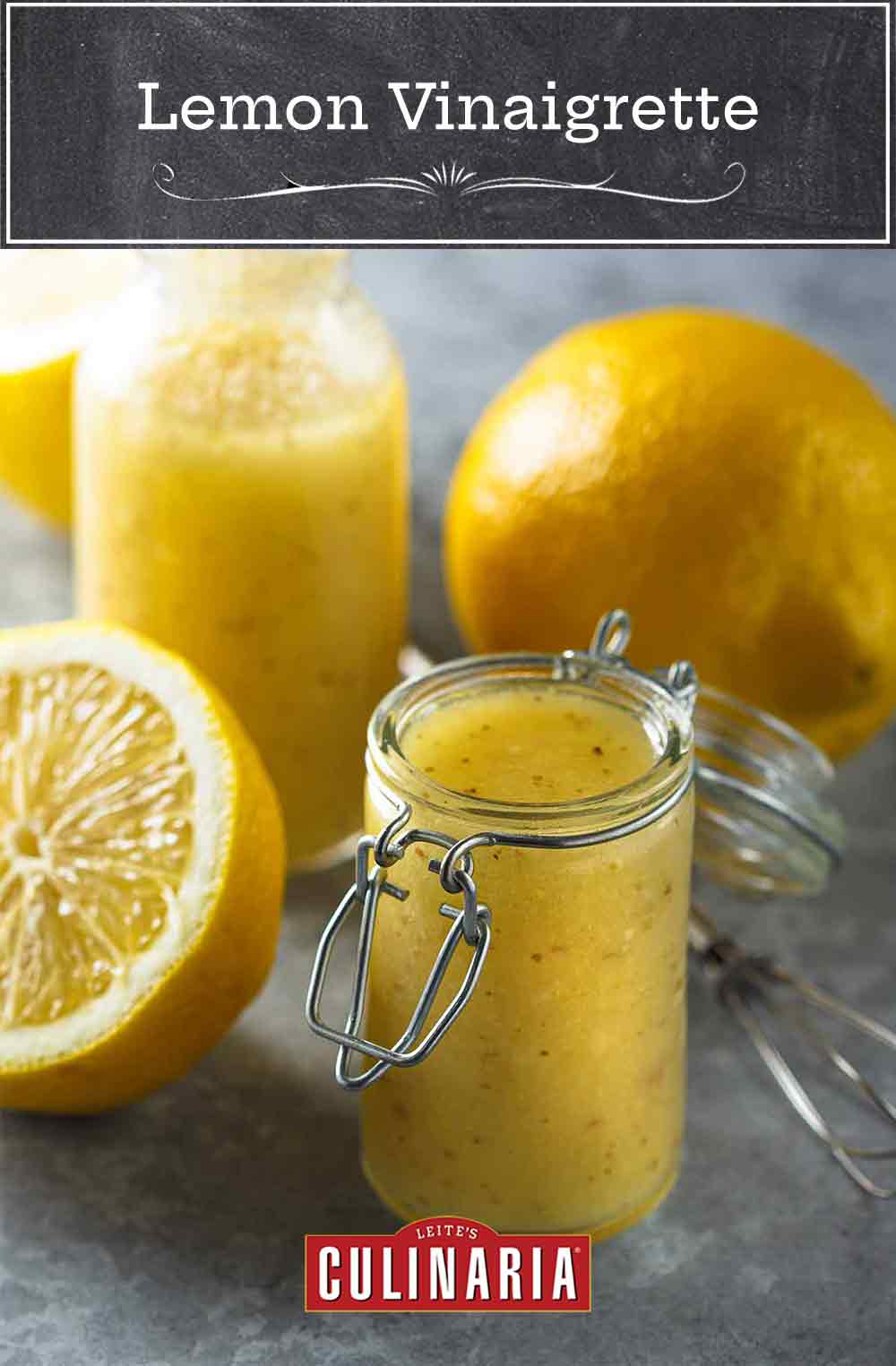 Two jars of lemon vinaigrette, two lemon halves, and a wire whisk.