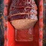 Half a cooked meatloaf in a red loaf tin with two slices cut from it.