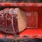 Half a cooked meatloaf in a red loaf tin with two slices cut from it.