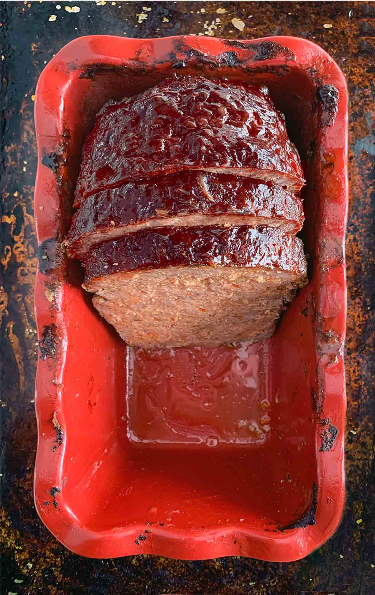 Half a cooked meatloaf in a red loaf tin with two slices cut from it.