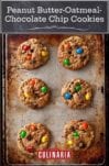 A baking sheet with six peanut butter-oatmeal-chocolate chip cookies studded with M&Ms