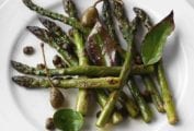 A white plate topped with roasted asparagus with bay leaves and crispy capers.