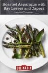 A white plate topped with roasted asparagus with bay leaves and crispy capers.