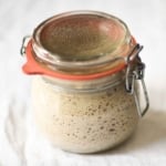 A glass jar filled with rye sourdough starter, sealed with a red rubber gasket.