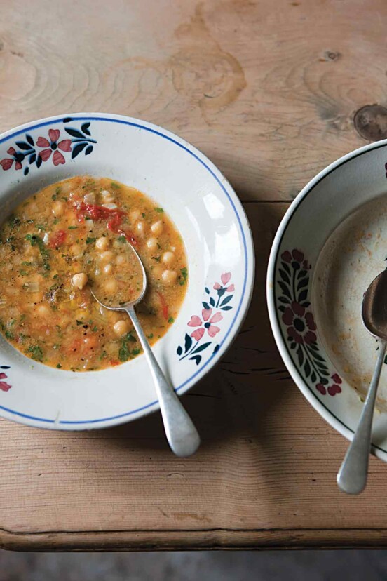 Two bowls, one filled with smoked paprika and chickpea soup, with a spoon resting inside, and the other bowl empty.