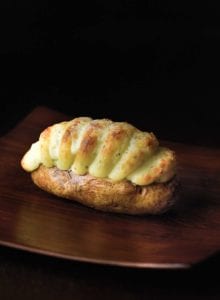 A twice-baked potato with Irish Cheddar on a dark wood table.
