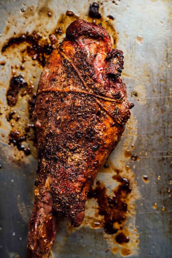 A tied whole roasted leg of lamb with a crispy garlic crust on a metal baking sheet.