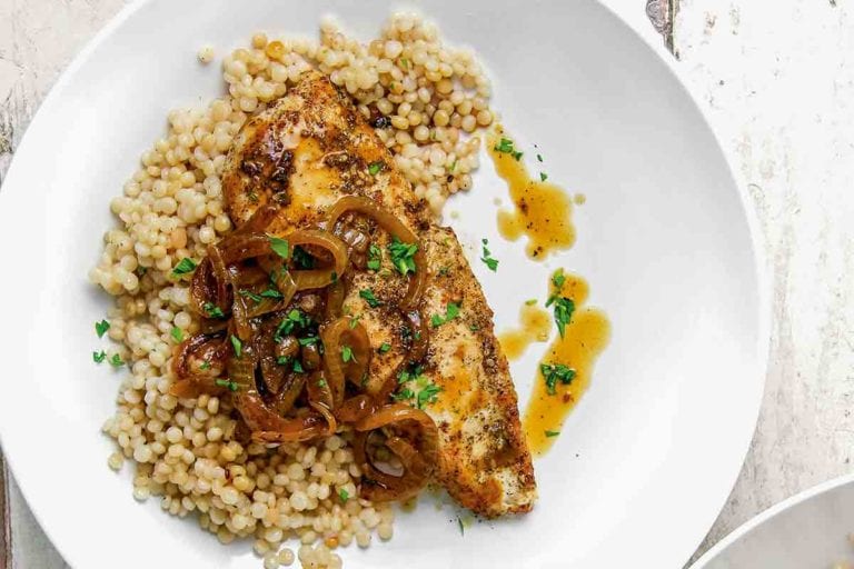 Two white plates each topped with a serving of za'atar chicken, Israeli couscous, sauteed onions, and pan juices.