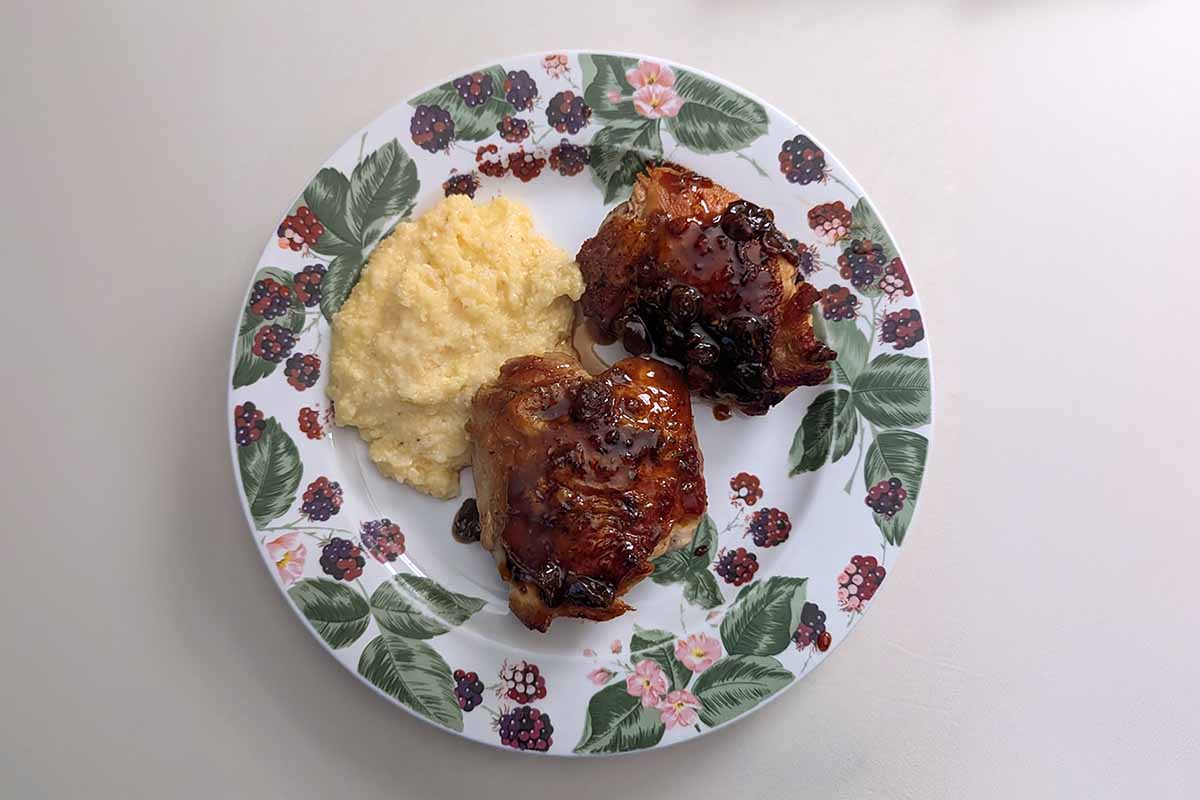 Agrodolce chicken thighs with garlic, rosemary, and golden raisins on a plate with polenta.