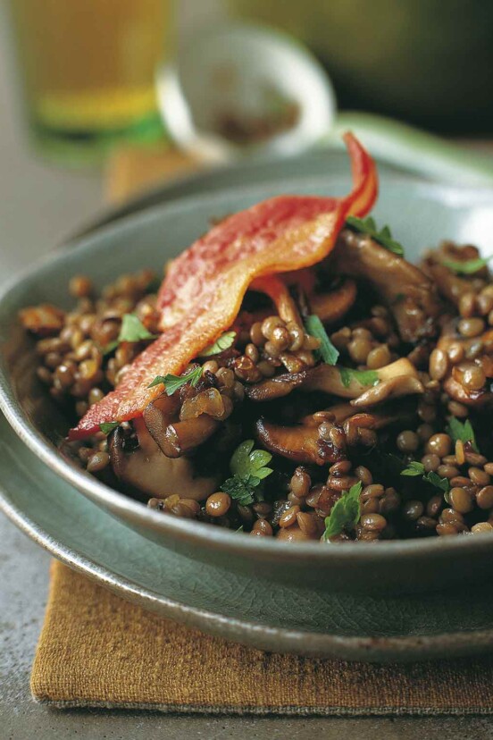A green bowl filled with sautéed bacon, mushrooms, and lentils with a whole piece of bacon on top.