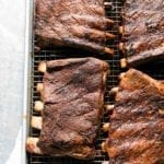 Four slabs of BBQ oven ribs on a rack inside a rimmed baking sheet.