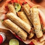 A basket of black bean taquitos with lime halves and hot sauce on the side.