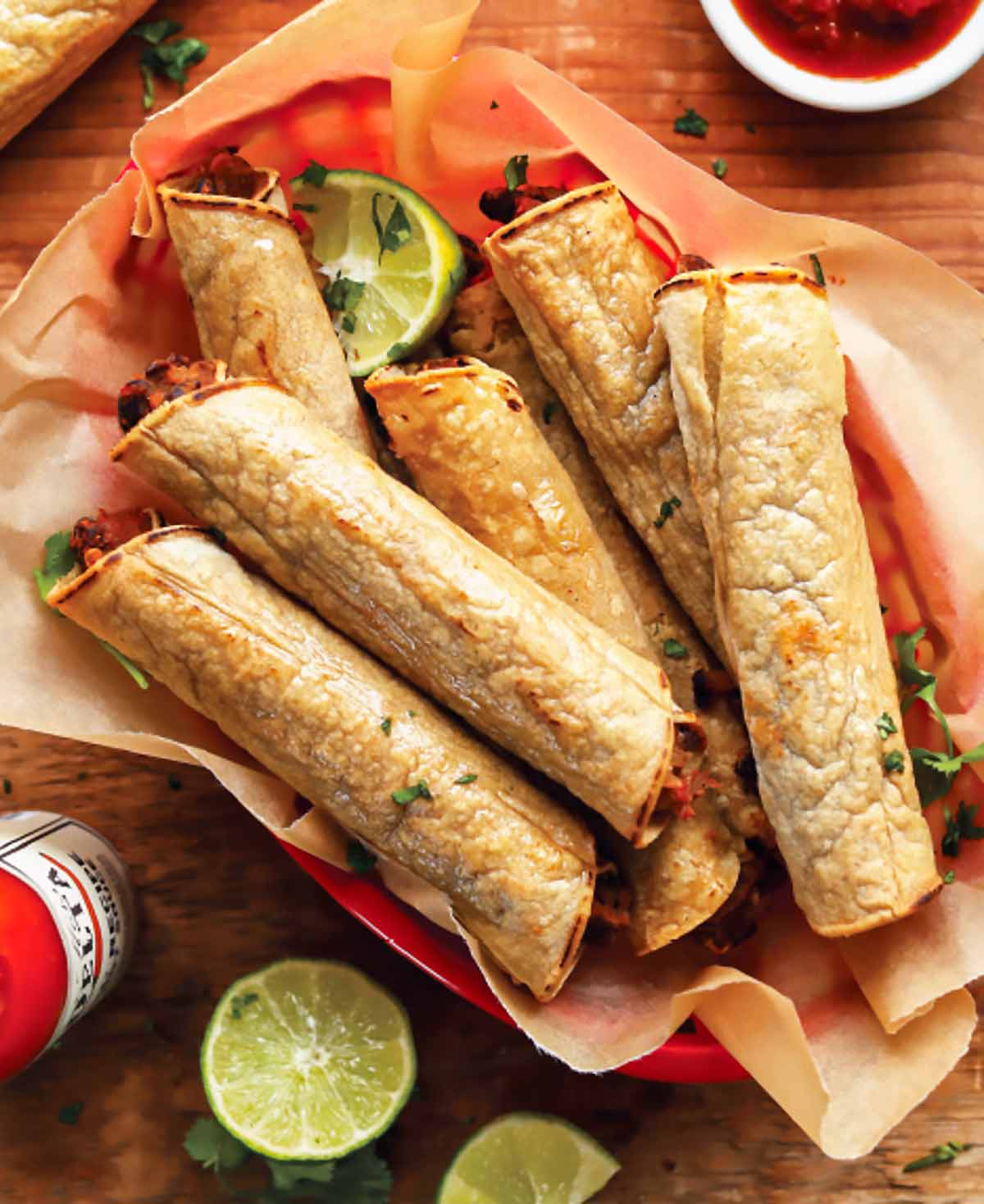 A basket of black bean taquitos with lime halves and hot sauce on the side.