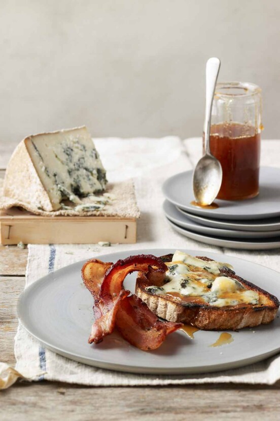 A piece of blue cheese tartine with two slices of crispy bacon on a grey plate.