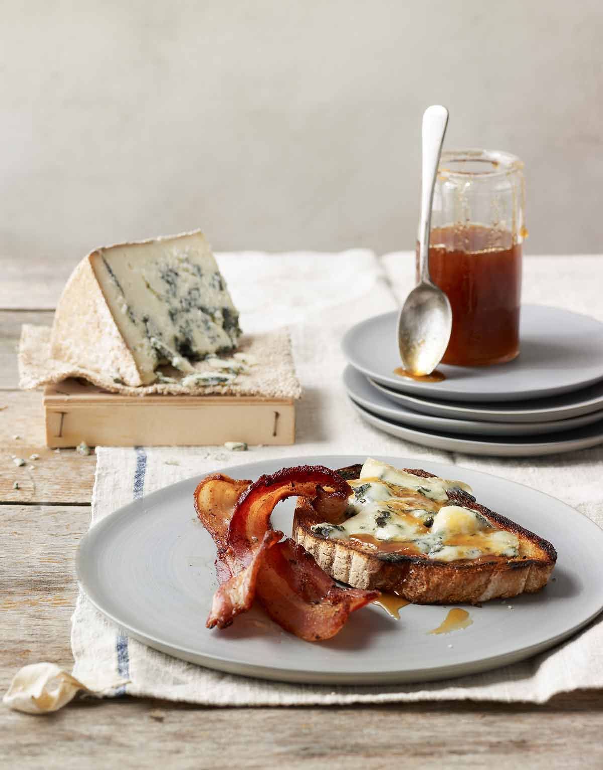 A piece of blue cheese tartine with two slices of crispy bacon on a grey plate.