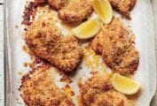 Six breaded oven fried chicken thighs with four lemon wedges in a parchment-lined dish.