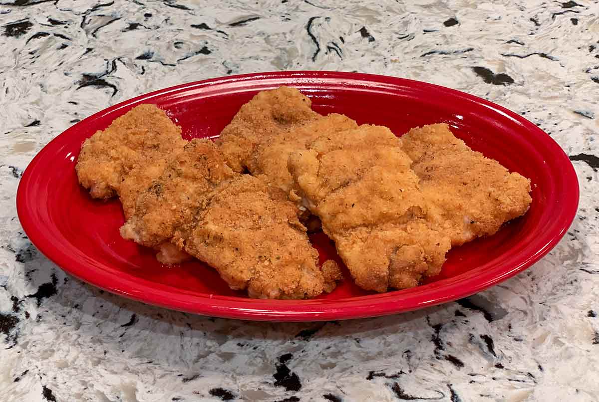 Four breaded oven fried chicken thighs on a red plate.