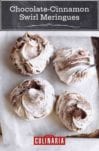 Four chocolate and cinnamon swirl meringues on a piece of parchment on a rimmed baking sheet.